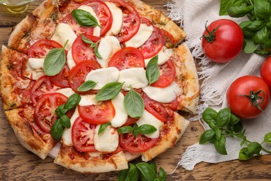 Photo of Delicious Caprese pizza with tomatoes, mozzarella and basil on wooden table, flat lay