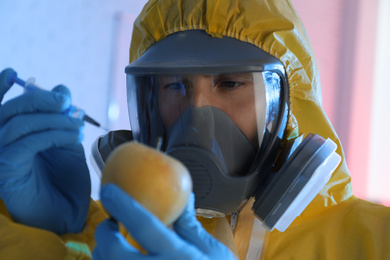 Photo of Scientist in chemical protective suit injecting apple on color background, closeup