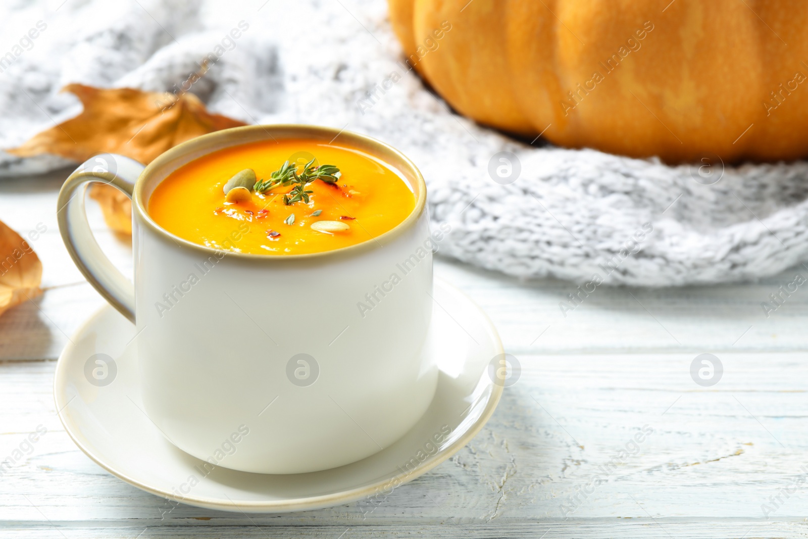 Photo of Delicious pumpkin soup in cup on white wooden table