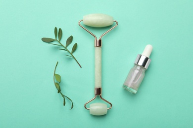 Photo of Natural face roller, cosmetic product and leaves on turquoise background, flat lay