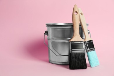 Photo of Bucket of paint and brushes on pink background. Space for text