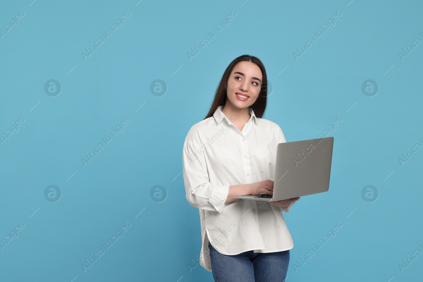 Photo of Smiling young woman with laptop on light blue background. Space for text