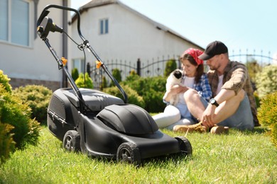 Happy couple with dog spending time in garden, focus on lawn mower