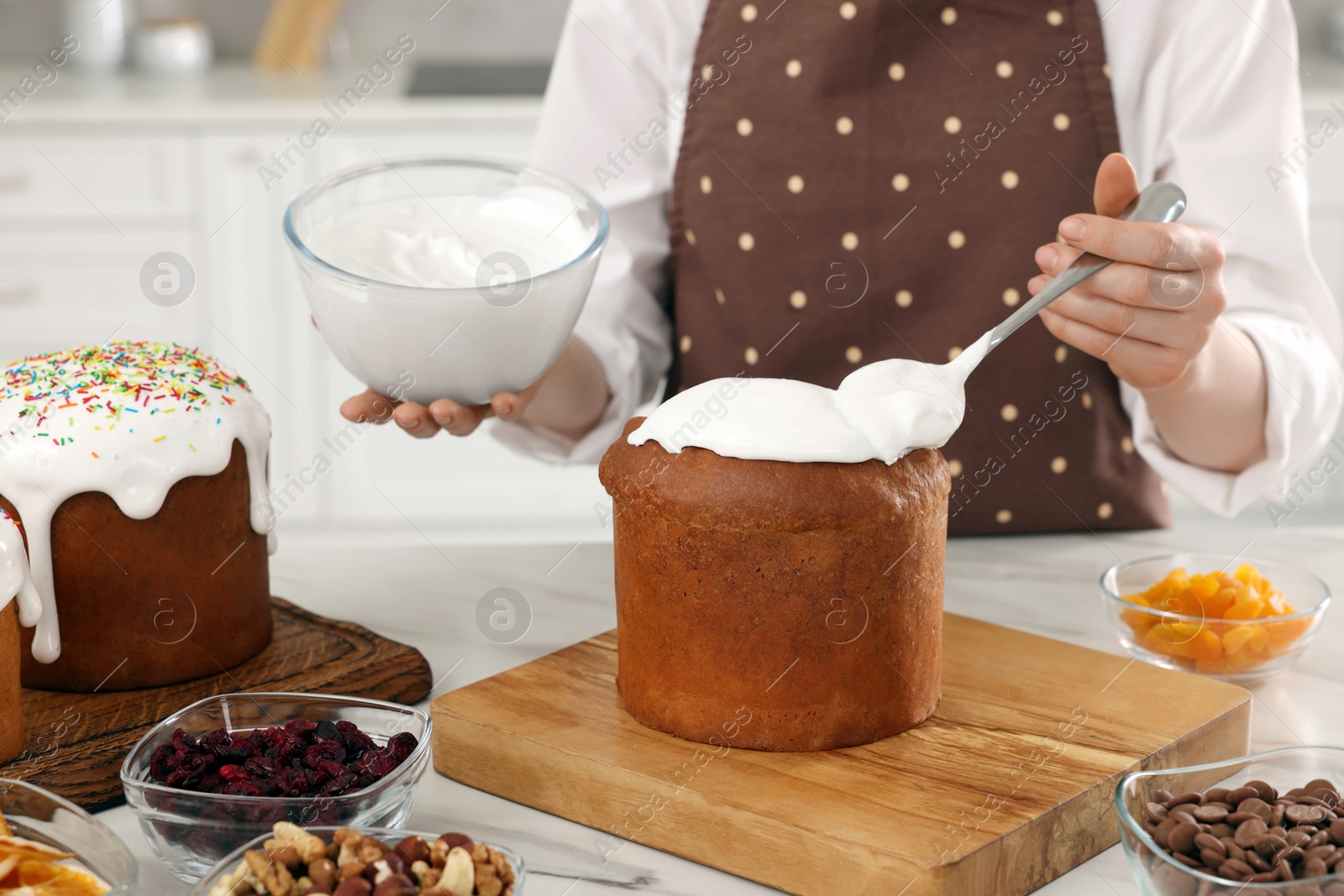 Photo of Woman decorating traditional Easter cake with glaze at white marble table in kitchen, closeup