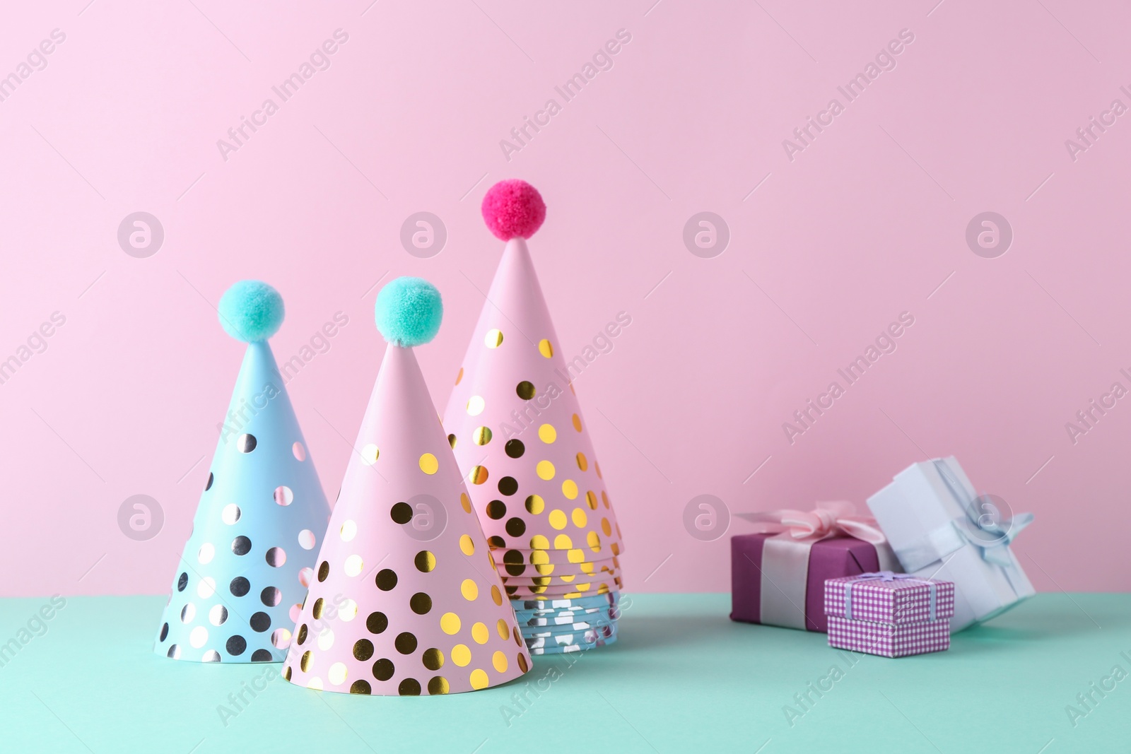 Photo of Party hats and gift boxes on color background