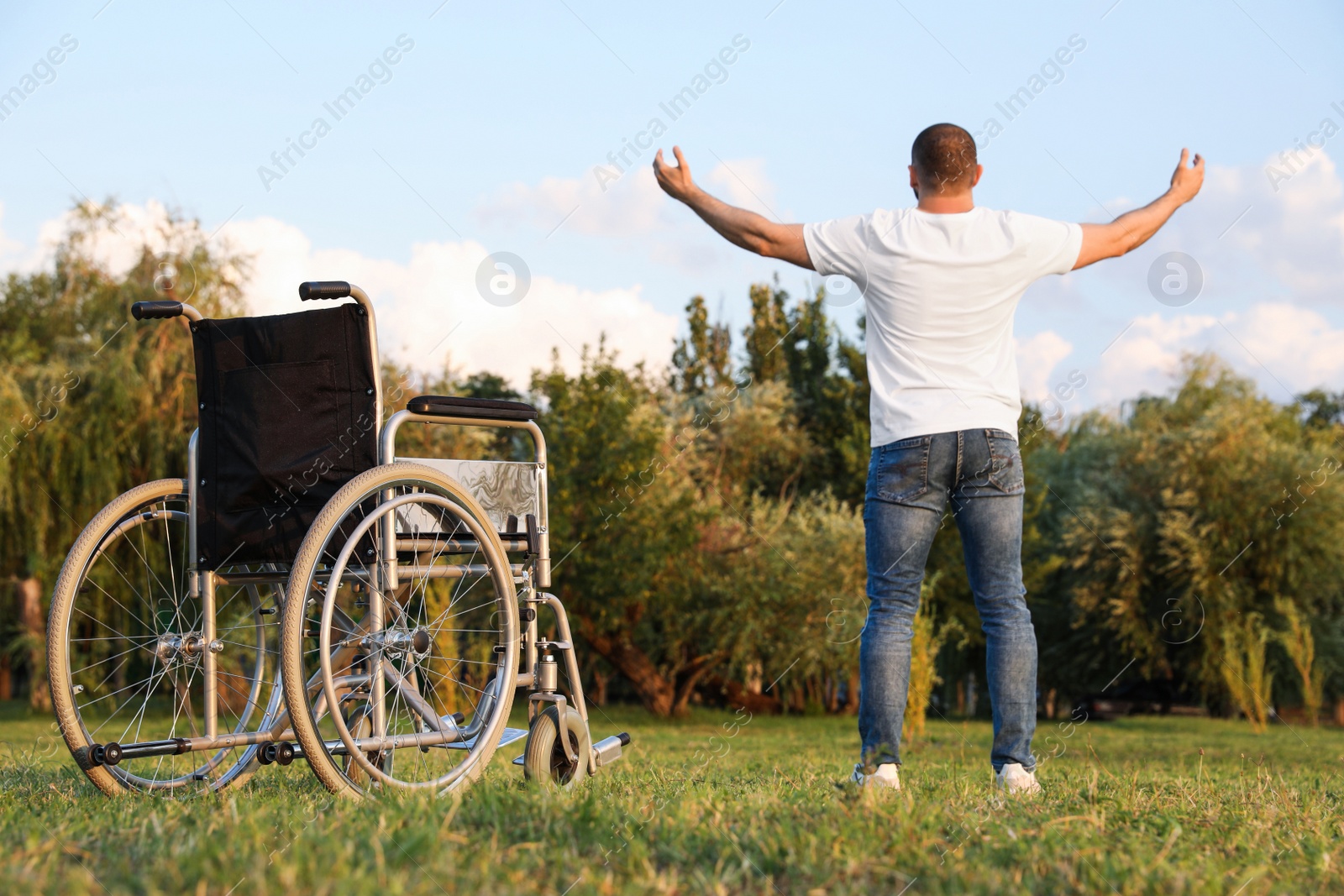 Photo of Man standing near wheelchair on sunny day, back view. Healing miracle