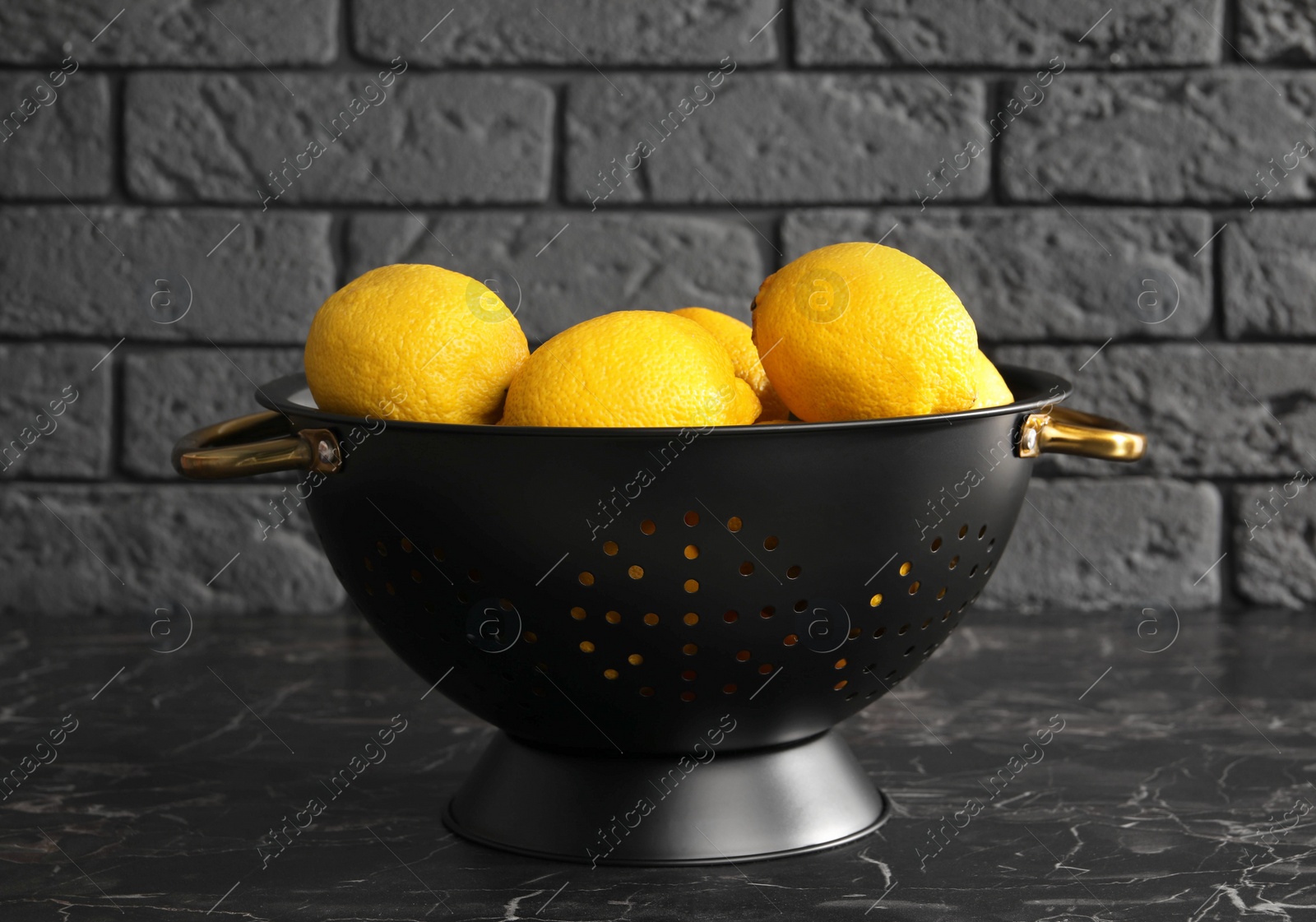 Photo of One colander with fresh lemons on black marble table