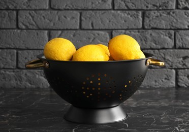 Photo of One colander with fresh lemons on black marble table