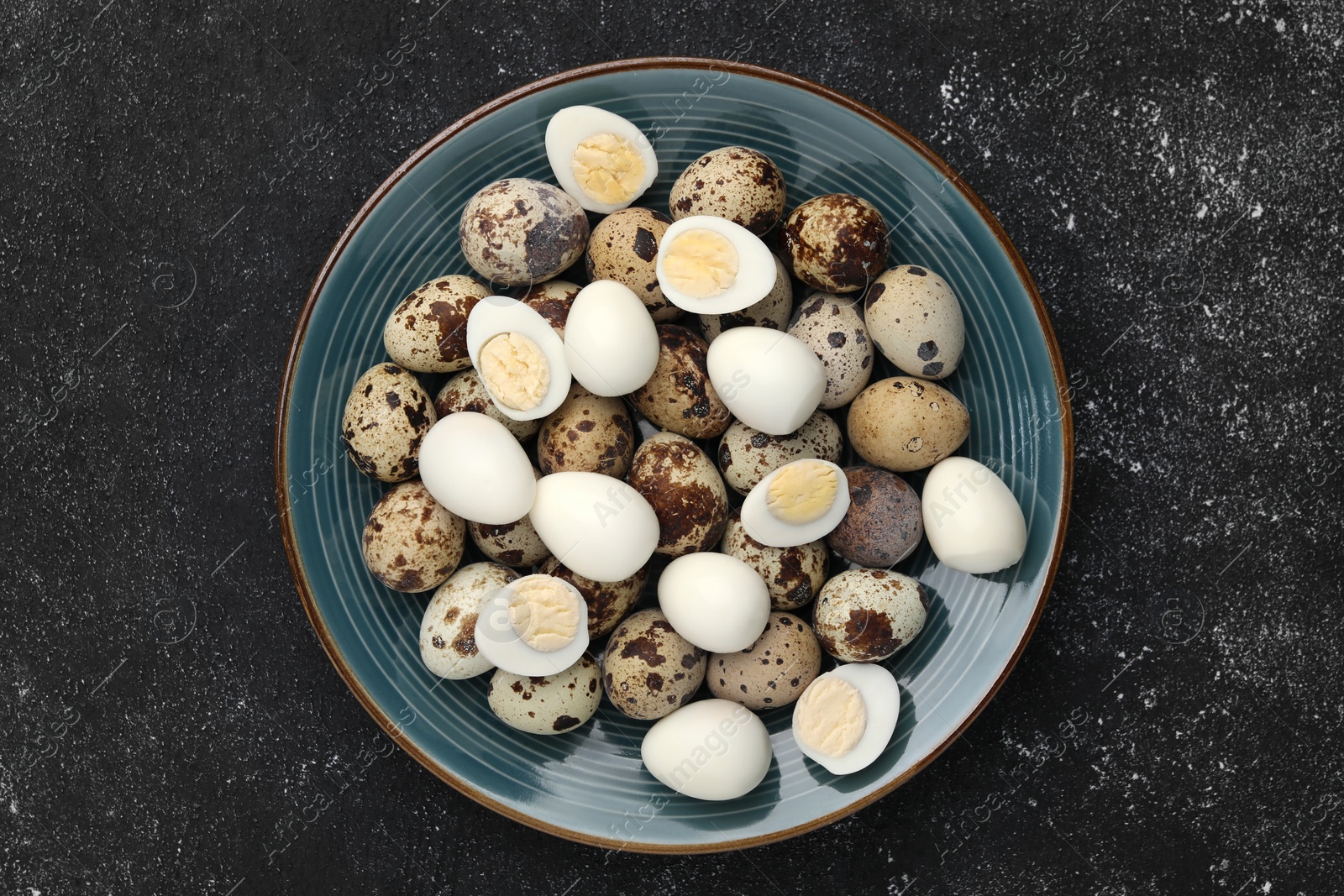 Photo of Peeled and unpeeled hard boiled quail eggs in plate on black table, top view
