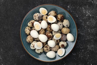 Peeled and unpeeled hard boiled quail eggs in plate on black table, top view