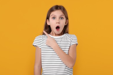 Surprised girl pointing at something on yellow background