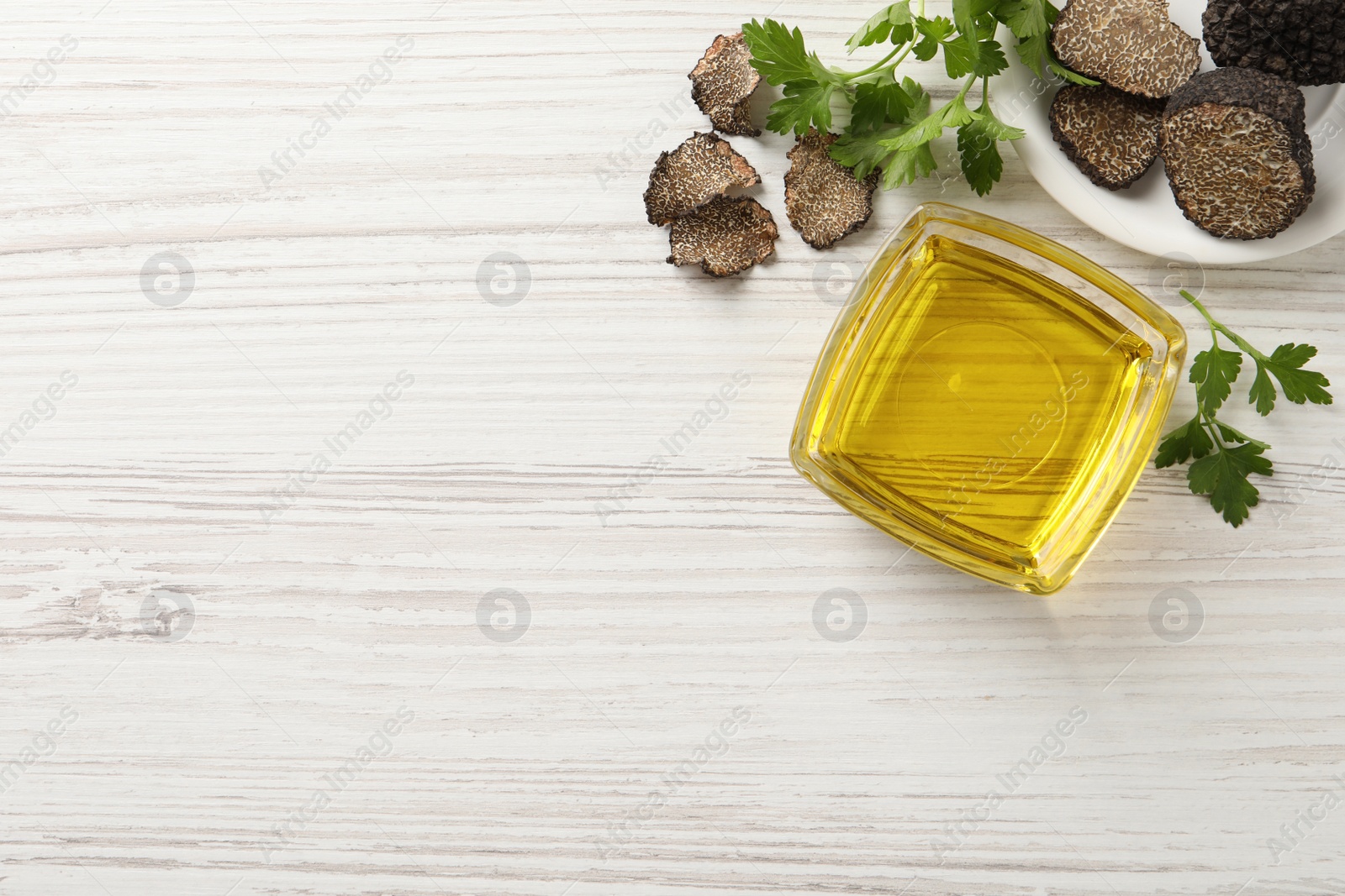 Photo of Fresh truffles, oil in glass bowl and parsley on white wooden table, flat lay. Space for text