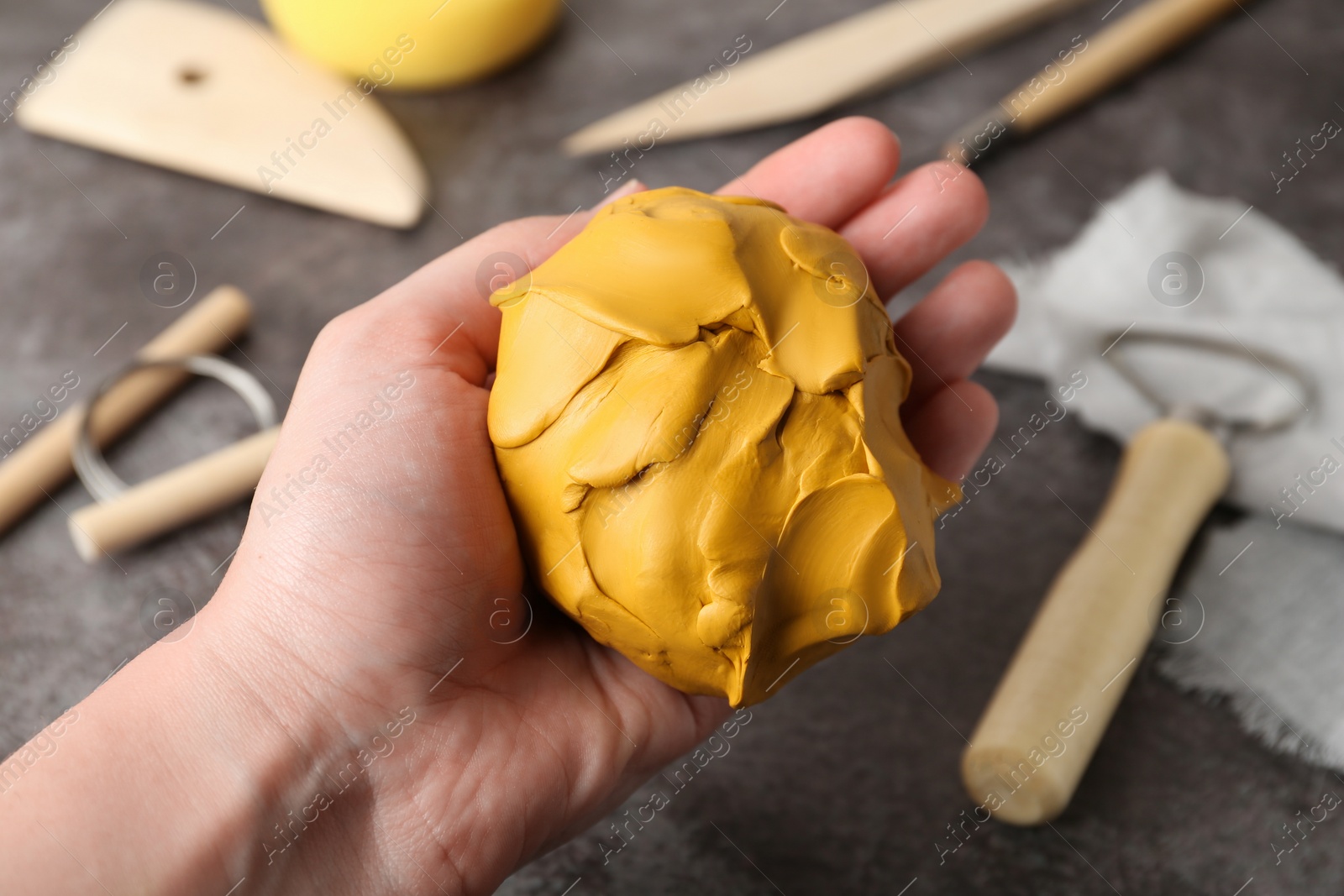 Photo of Woman holding clay over grey stone table with modeling tools, closeup