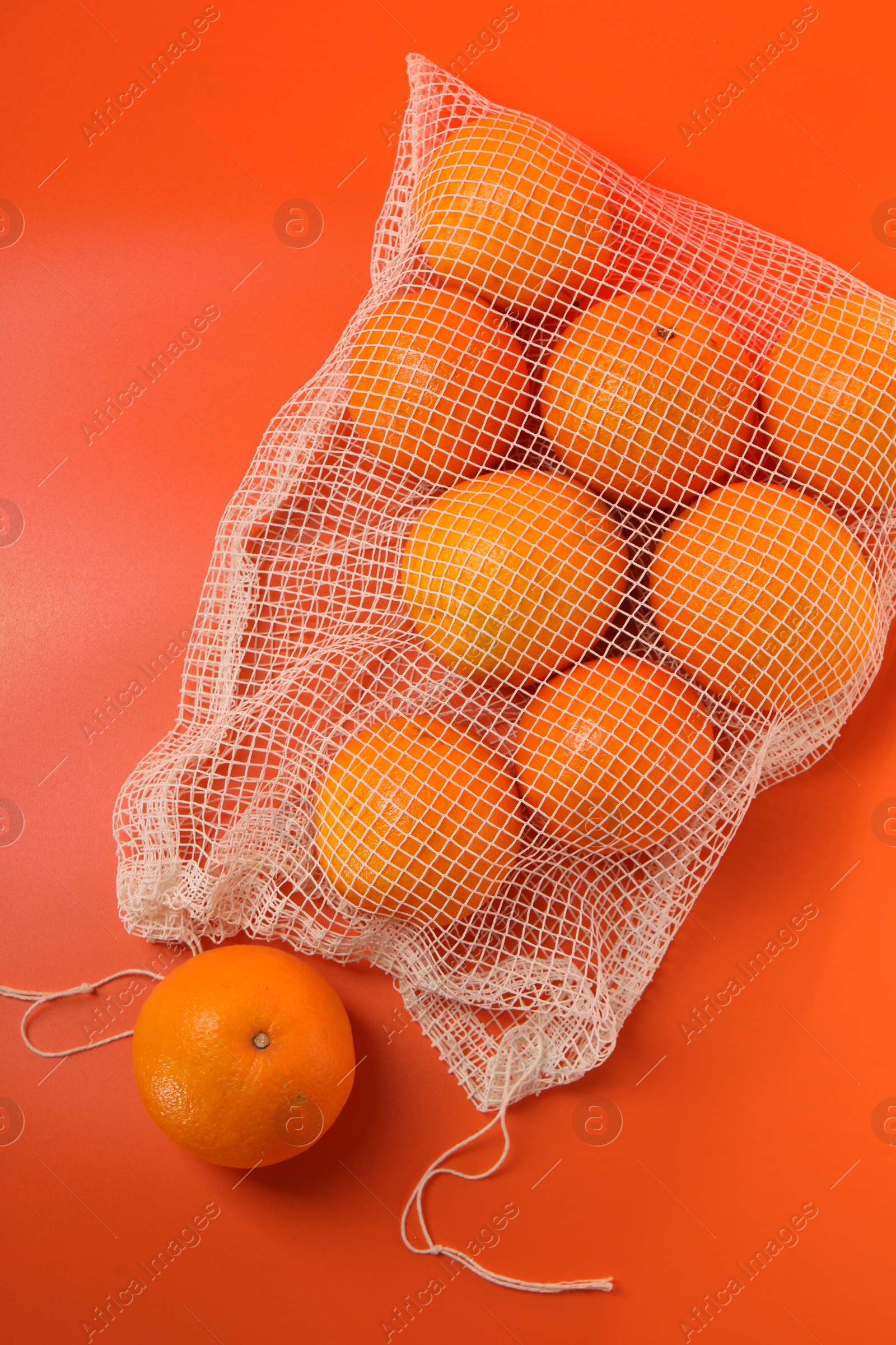 Photo of Net bag with fresh oranges on color background, top view