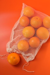 Net bag with fresh oranges on color background, top view