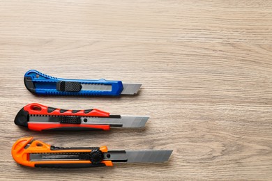 Photo of Different utility knives on wooden table, flat lay. Space for text