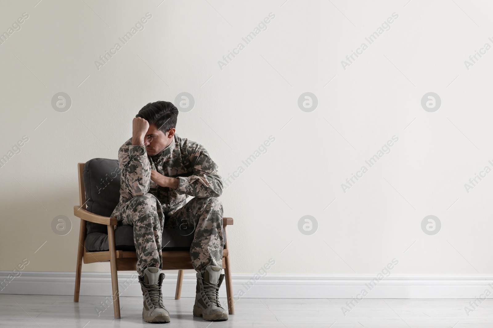 Photo of Stressed military officer sitting in armchair near white wall indoors. Space for text