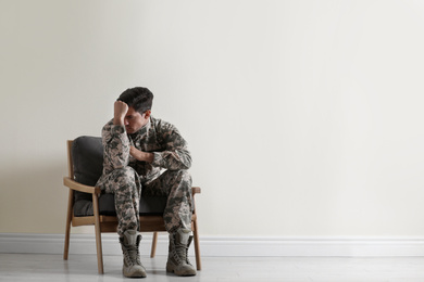 Stressed military officer sitting in armchair near white wall indoors. Space for text