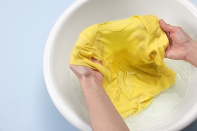 Photo of Woman washing baby clothes in basin on light blue background, top view