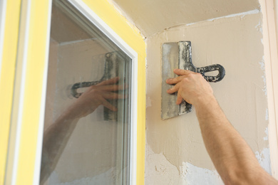Photo of Man plastering window area with putty knife indoors, closeup. Interior repair