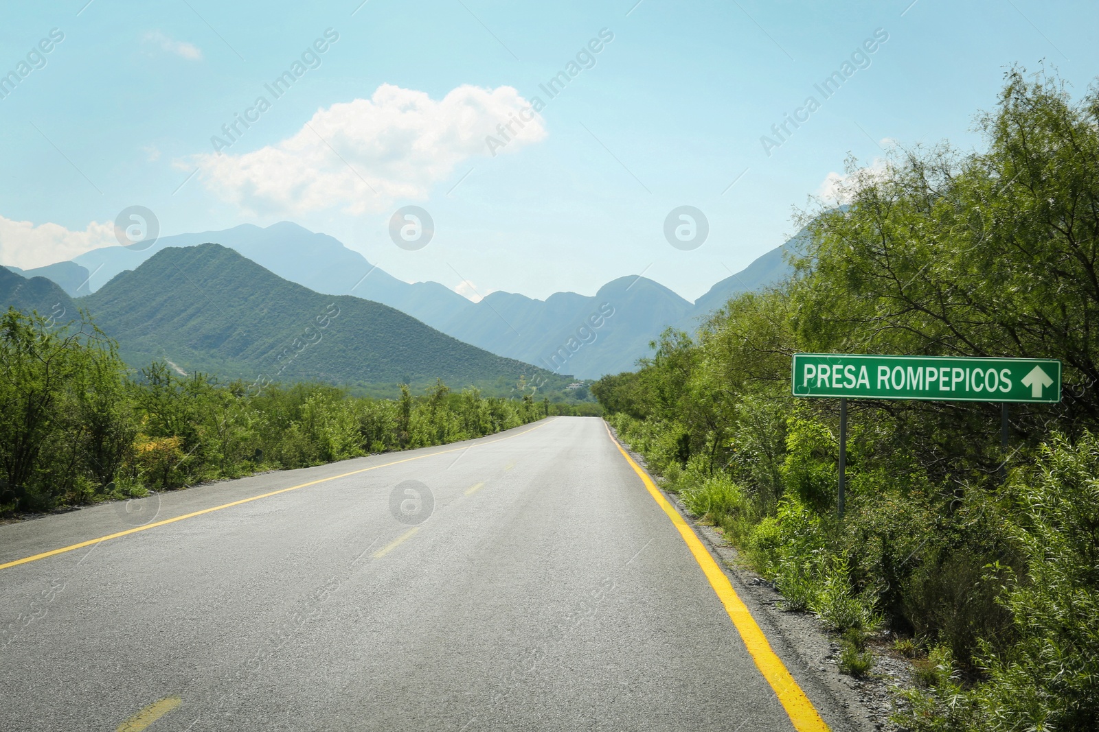 Photo of Picturesque view of big mountains and bushes near road under bright sky