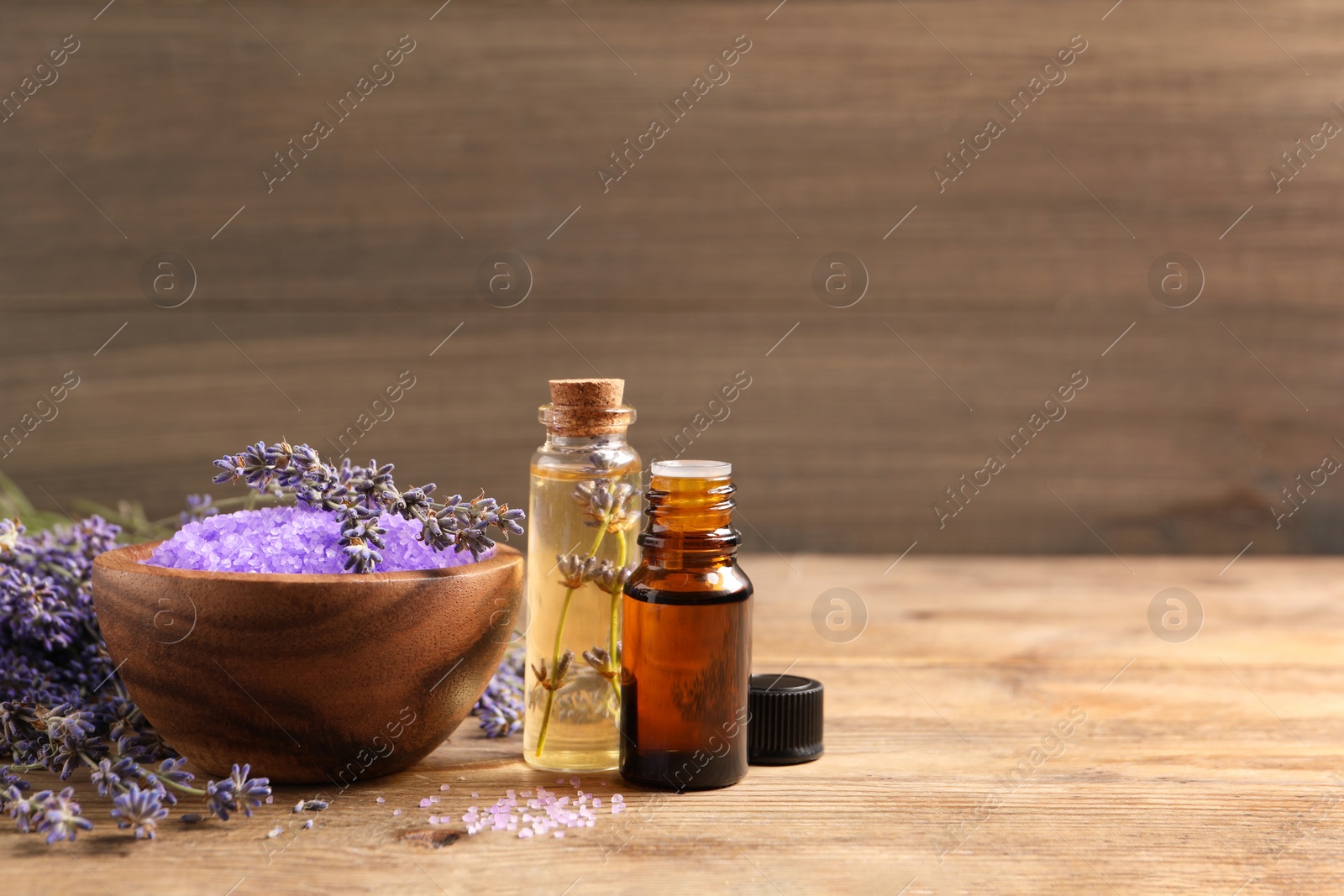 Photo of Bowl of sea salt, essential oil and lavender flowers on wooden table, space for text