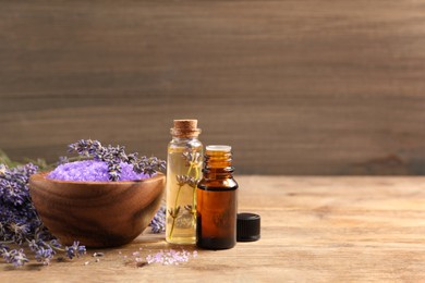 Bowl of sea salt, essential oil and lavender flowers on wooden table, space for text