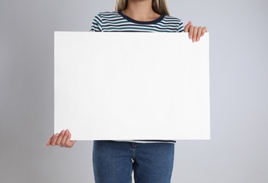 Woman holding blank poster on light grey background, closeup