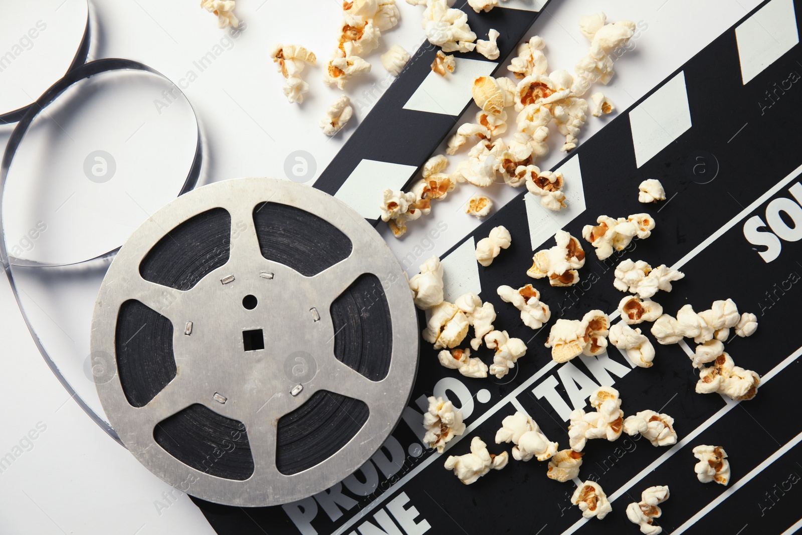 Photo of Tasty popcorn, film reel and clapperboard on white background, top view. Cinema snack