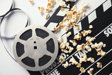 Photo of Tasty popcorn, film reel and clapperboard on white background, top view. Cinema snack