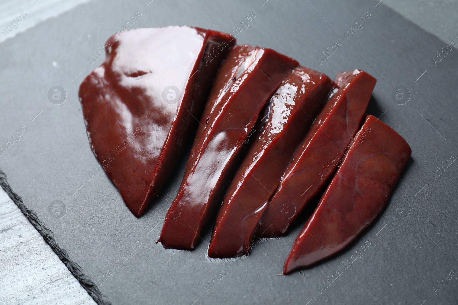 Photo of Cut raw beef liver on black table, closeup