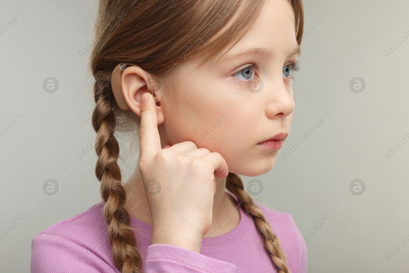 Photo of Little girl with hearing aid on grey background, closeup