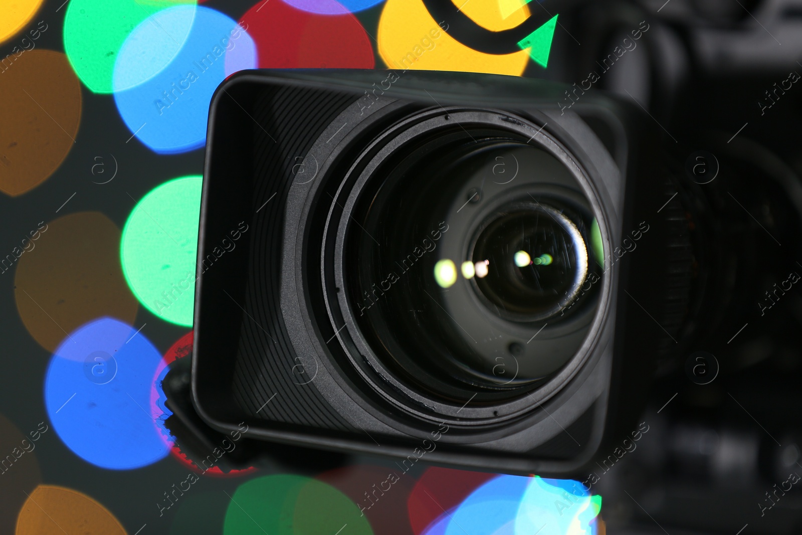 Photo of Modern video camera against blurred colorful lights, closeup