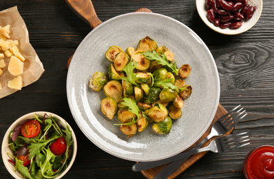 Photo of Delicious roasted brussels sprouts with arugula served on black wooden table, flat lay