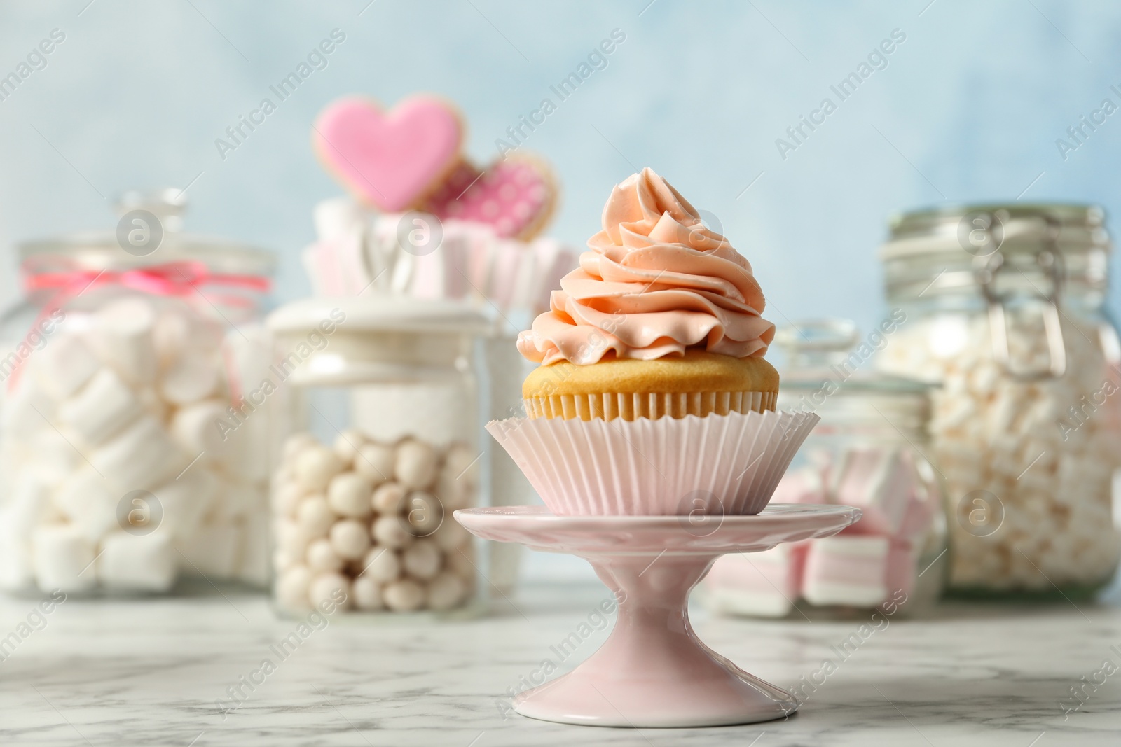 Photo of Stand with cupcake and other sweets on white marble table. Candy bar