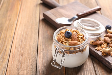 Photo of Jar with yogurt, nuts and granola on wooden table