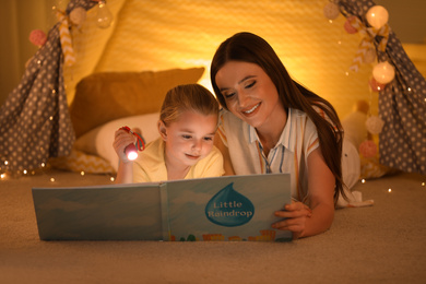 Mother and daughter with flashlight reading book at home