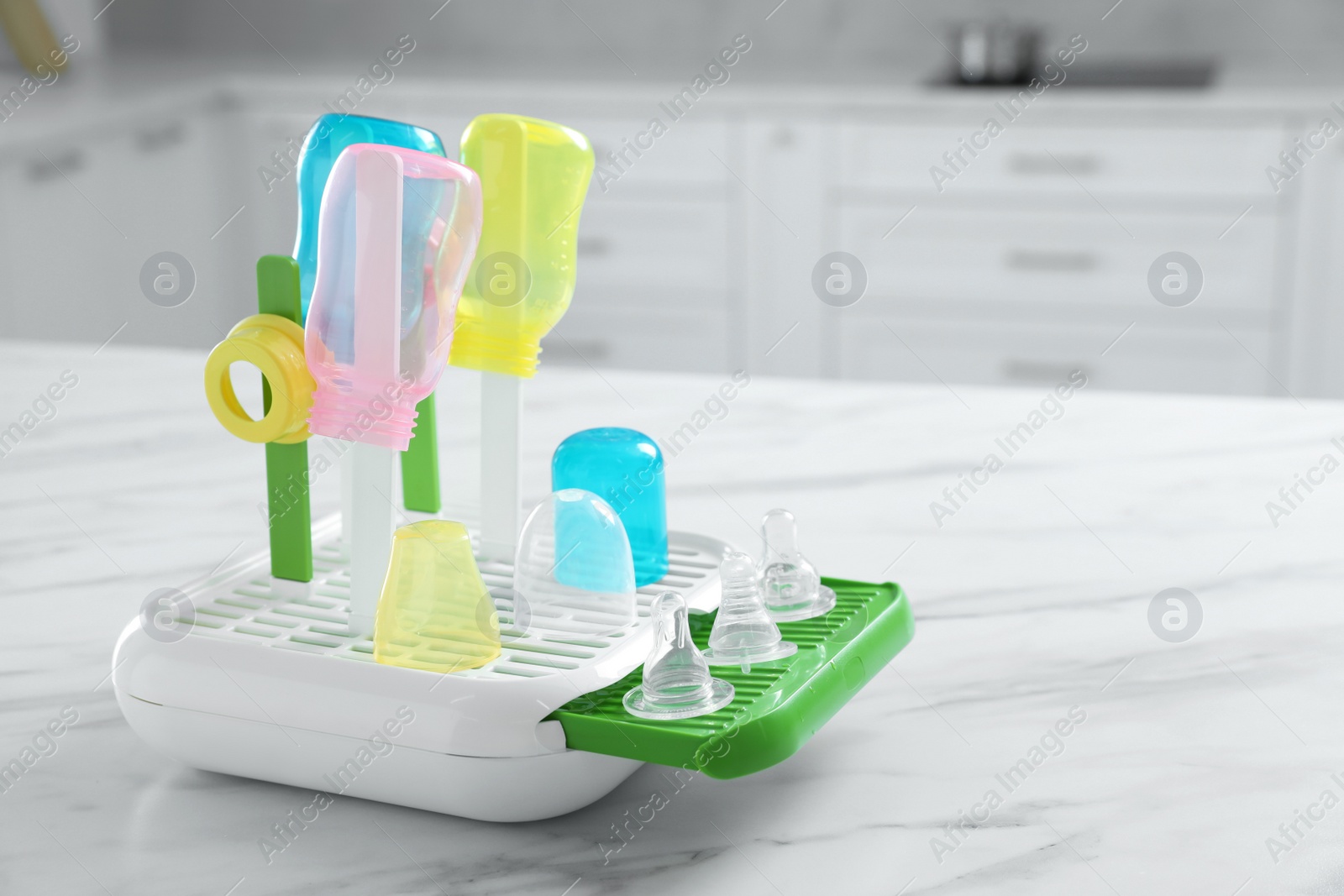 Photo of Dryer with baby bottles and nipples after sterilization on white marble table in kitchen. Space for text