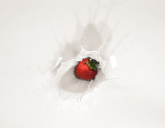 Strawberry falling in milk with splash, top view