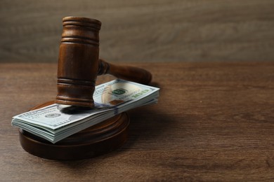 Photo of Law gavel with stack of dollars on wooden table, closeup. Space for text