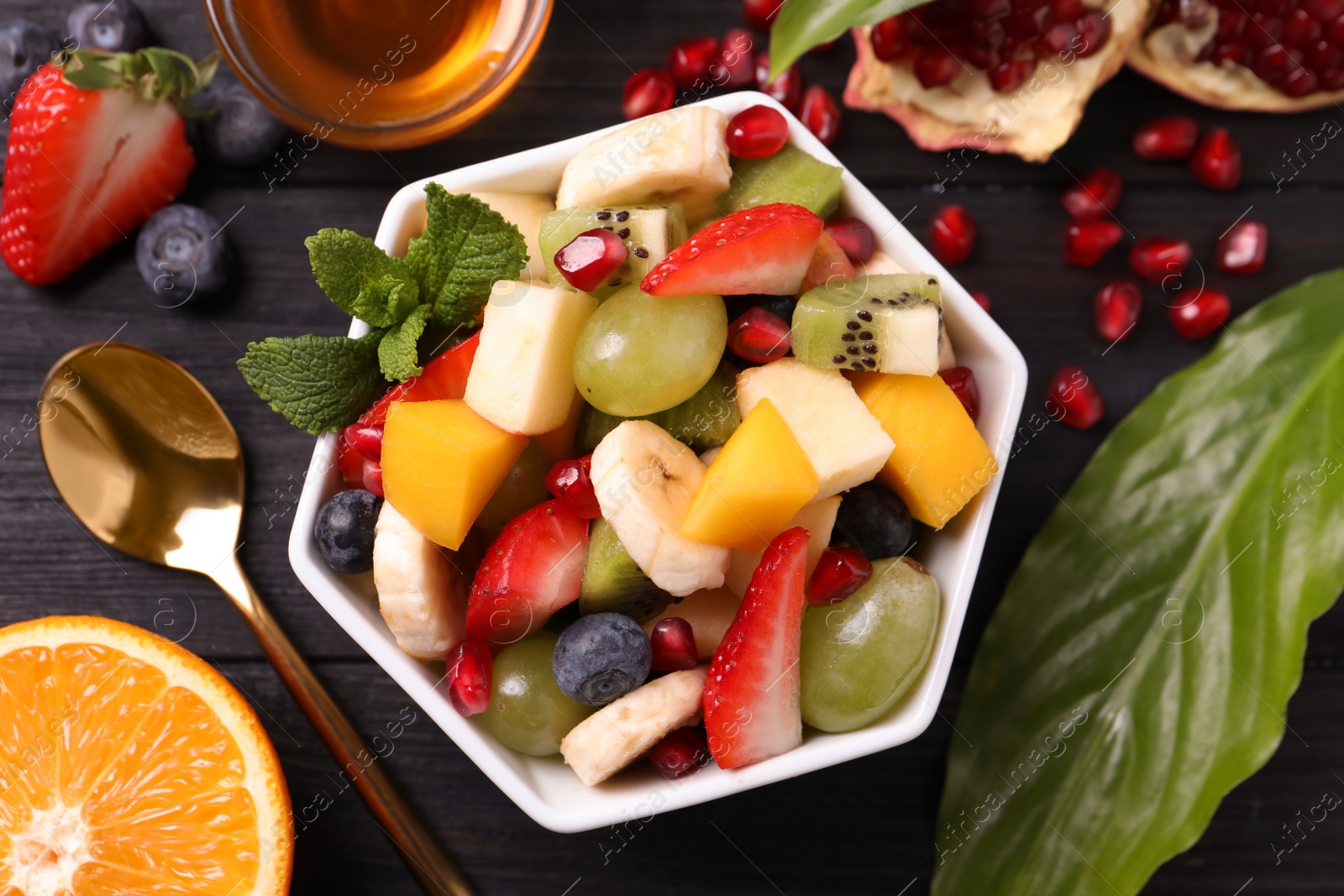 Photo of Delicious fresh fruit salad in bowl on black wooden table, flat lay