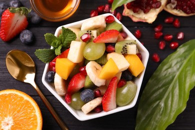 Photo of Delicious fresh fruit salad in bowl on black wooden table, flat lay