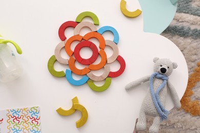 Photo of Colorful wooden pieces of playing set and toy bear on white table, flat lay. Motor skills development