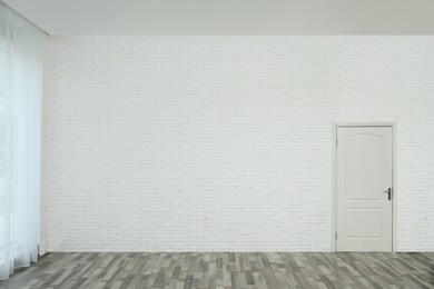 Photo of Empty room with brick wall, white door and laminated floor