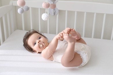 Photo of Cute little baby lying in crib with hanging mobile