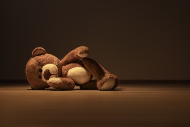 Photo of Cute teddy bear left on floor in dark room. Space for text