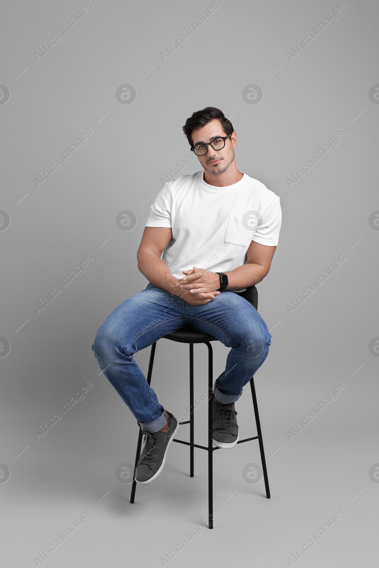 Photo of Handsome young man sitting on stool against grey background