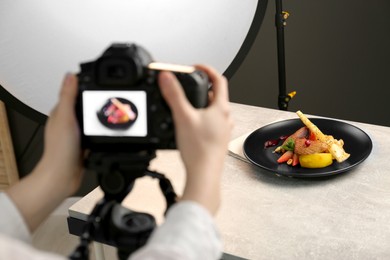 Photo of Woman taking picture of dish with chicken, parsnip and strawberries on grey table in professional photo studio, closeup. Food stylist