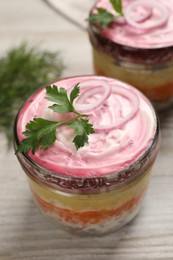 Glass jars of herring under fur coat on wooden table, closeup. Traditional Russian salad