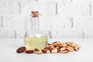 Photo of Tasty Brazil nuts and bottle with oil on white table against brick wall. Space for text